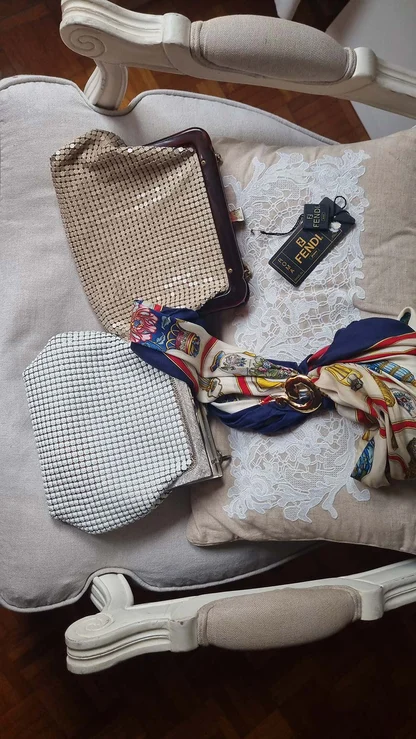 Beige and white mesh bags on a cream armchair beside a silk scarf with a gold ring and a Fendi tag
