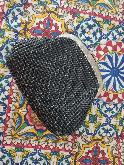 Black mesh clutch with a silver-tone frame, lying on a bright blue, red and yellow tile-print cloth