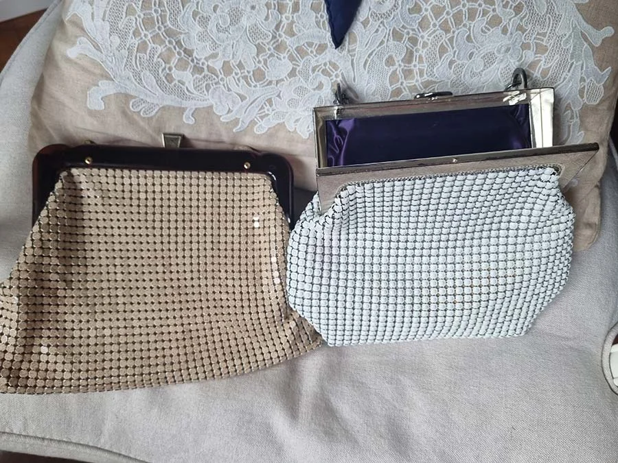Two vintage mesh evening bags on a lace cushion: a beige one with a dark frame and a white one with a silver frame
