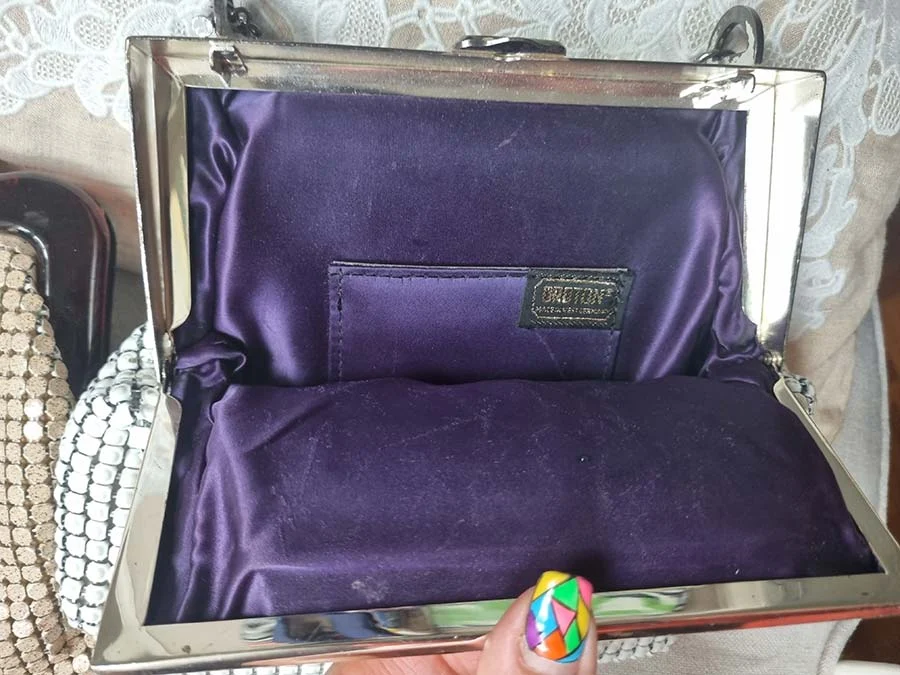 Inside a white mesh bag with a silver frame: purple satin lining and a small brand label