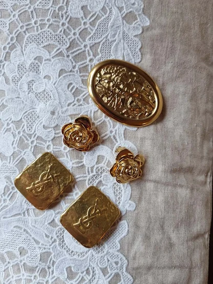 Gold Yves Saint Laurent logo earrings, gold rose earrings and an oval embossed brooch on white lace