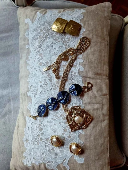 Gold-tone 1980s YSL jewellery on a lace cushion: blue enamel bracelet, pearl earrings, a brooch and square earrings