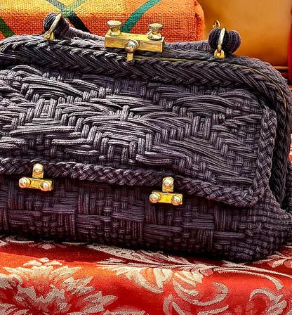 Close view of the dark woven bag's braided trim and brass clasps, set against red and gold damask