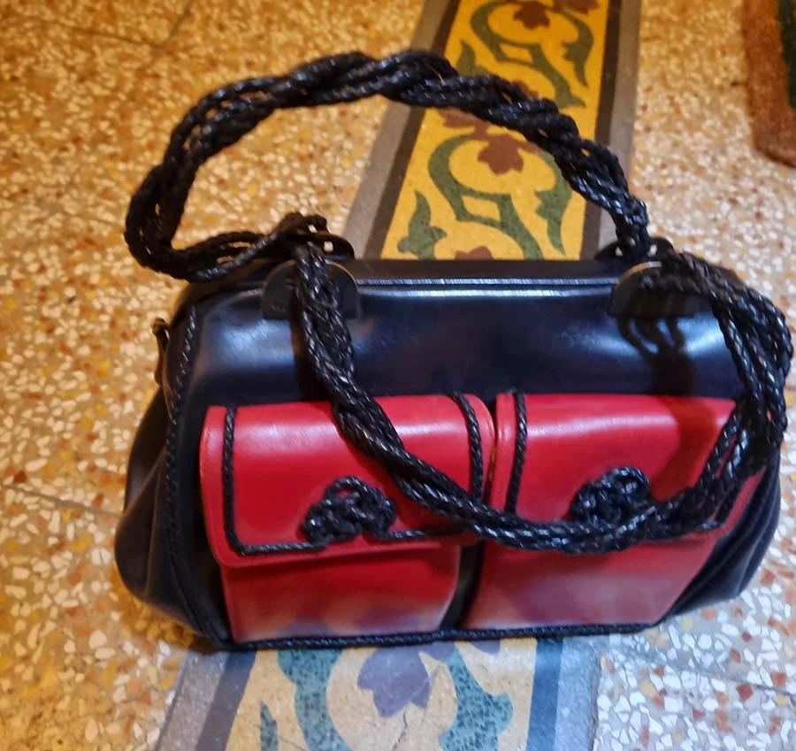 Roberta di Camerino black and red leather bag with two red front pockets and braided leather handles, on a tiled floor