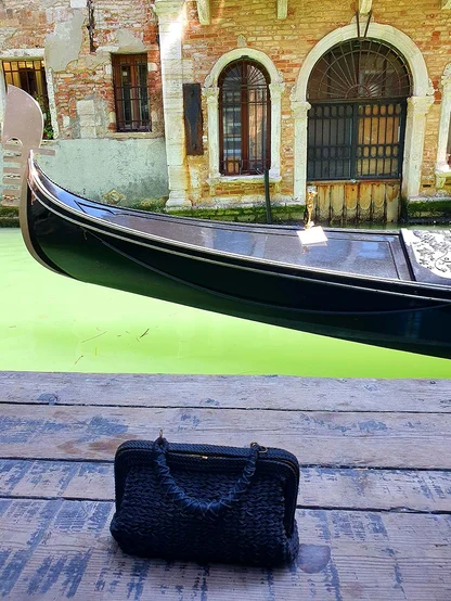 A black woven vintage bag on a wooden landing beside a gondola on a Venetian canal