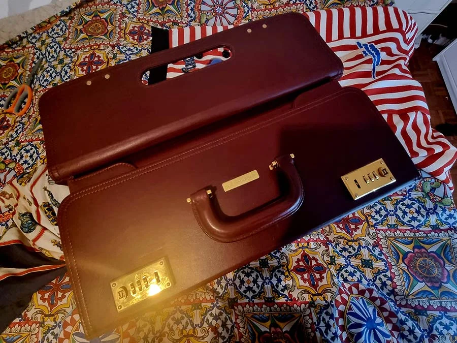 Burgundy Les Must de Cartier leather case open on a patterned cloth, with gold combination locks and a rounded handle