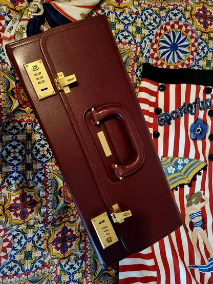 Burgundy Cartier case seen from above, with brass combination locks and handle, on blue and yellow tile-print fabric