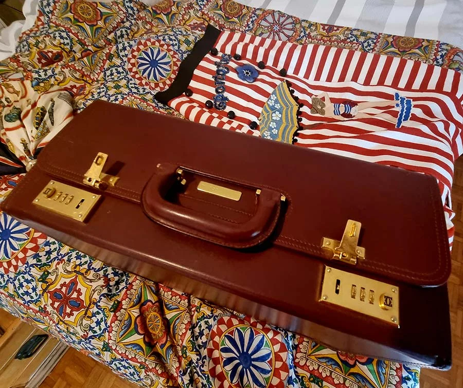 Closed burgundy leather Cartier case with brass clasps and a nameplate, beside a red and white striped garment