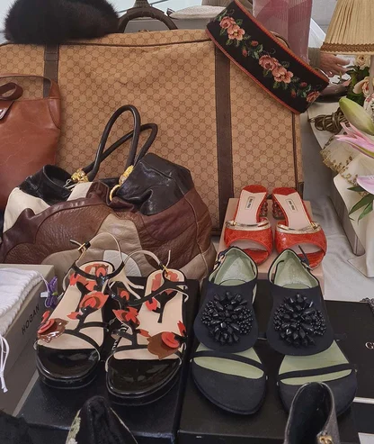 Market table of shoes and bags: red patterned mules, beaded black sandals, floral sandals and a monogram holdall