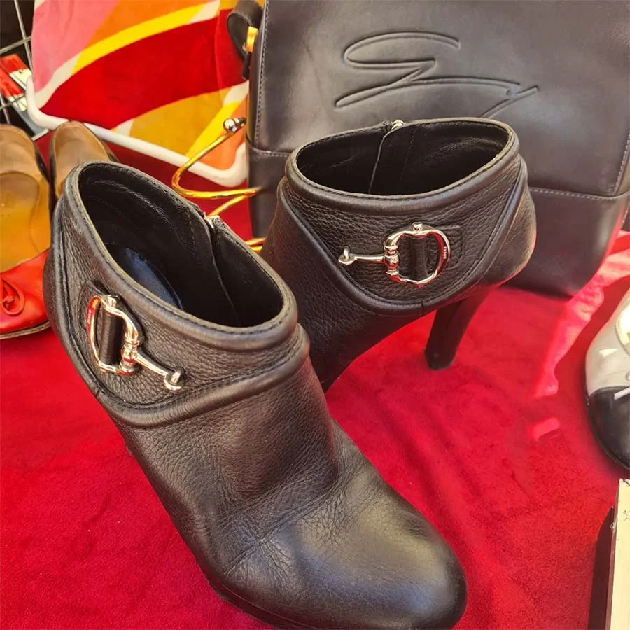 Black leather high-heeled ankle boots with a silver horsebit buckle, on a red cloth at a market stall