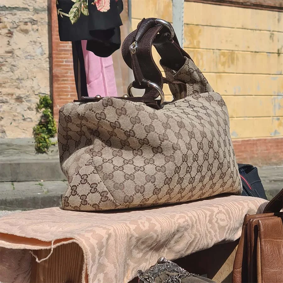 Gucci monogram canvas shoulder bag with a dark leather strap, on a pink damask cloth in front of a yellow wall