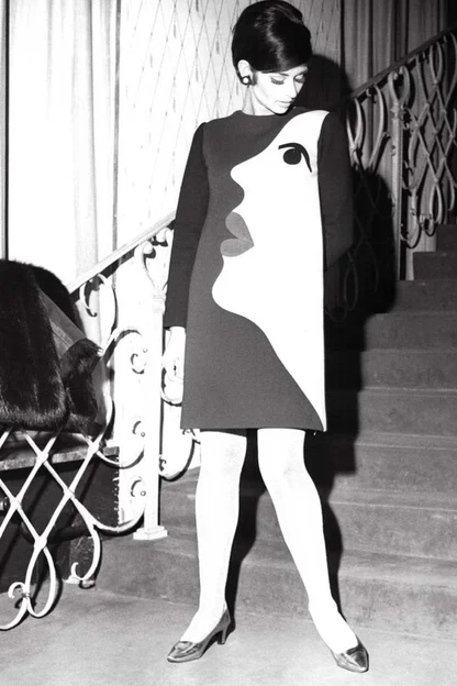 Woman on a staircase in a black and white shift dress with a stylised face appliquéd on the front