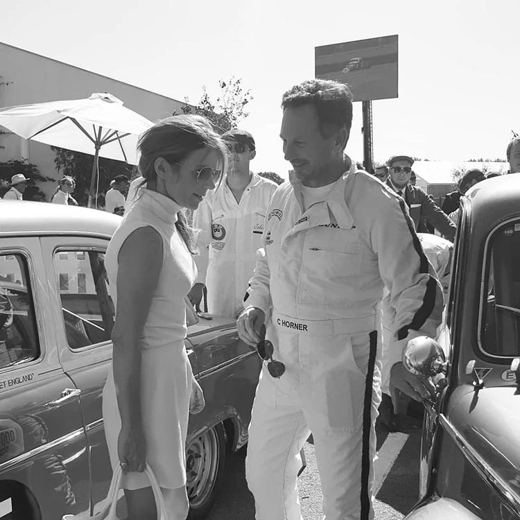 Geri Horner talking with Christian Horner, in white racing overalls, among vintage cars at Goodwood Revival
