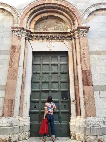 Gracie Opulanza in a floral top, cuffed Levi's and a red bag, facing a tall green door in a marble church front