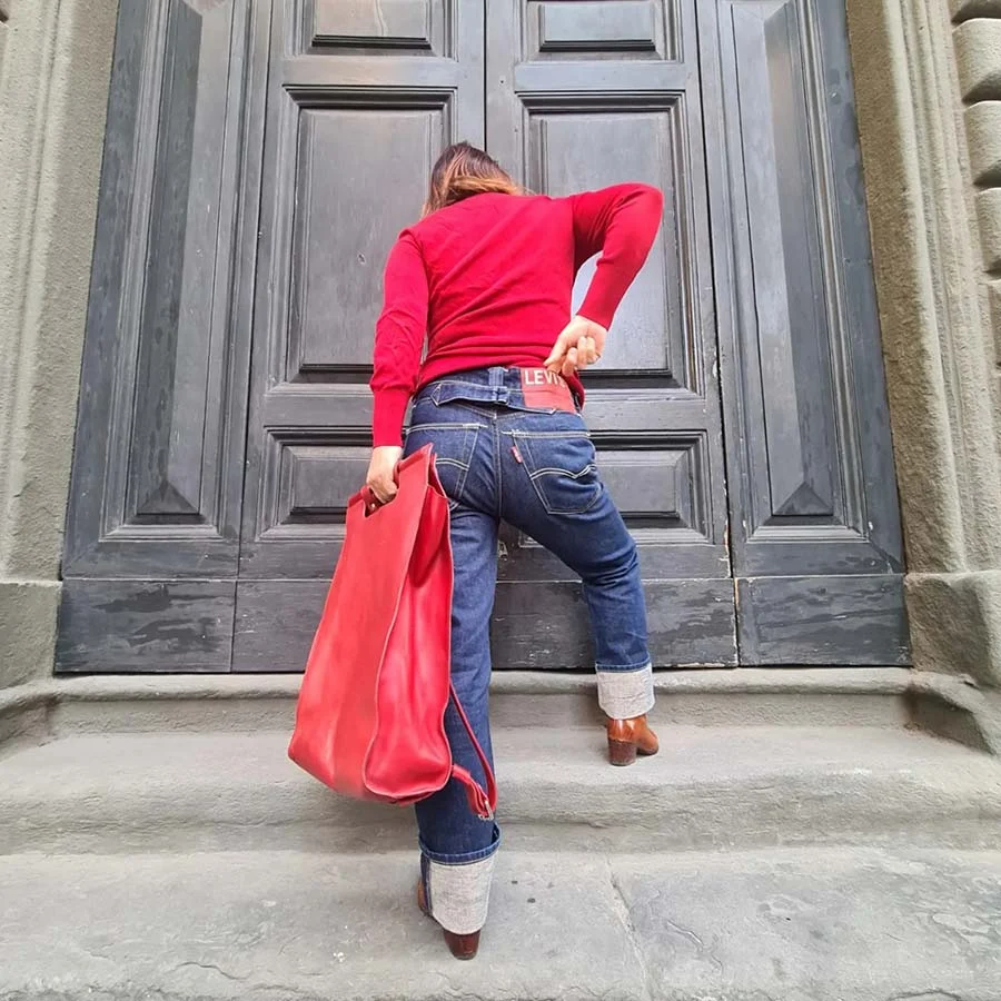 Gracie Opulanza from behind in a red jumper and Levi's, a hand on her back pocket, stepping up to grey panelled doors