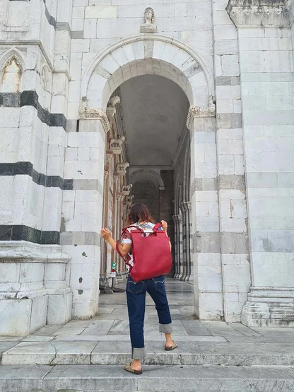 Gracie Opulanza in cuffed Levi's and a red backpack, walking up steps to a striped marble archway in Lucca