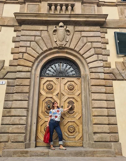 Gracie Opulanza in a floral top and cuffed Levi's, with a red bag, in front of an arched doorway with an iron fanlight