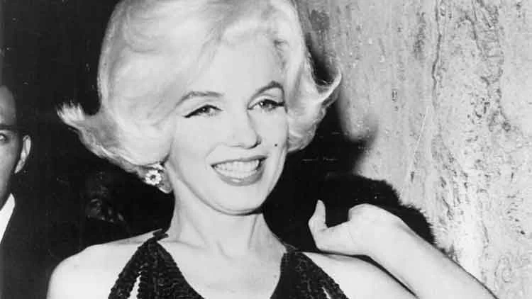 Marilyn Monroe smiling in a beaded dark halter top and drop earring, in a black-and-white press photograph