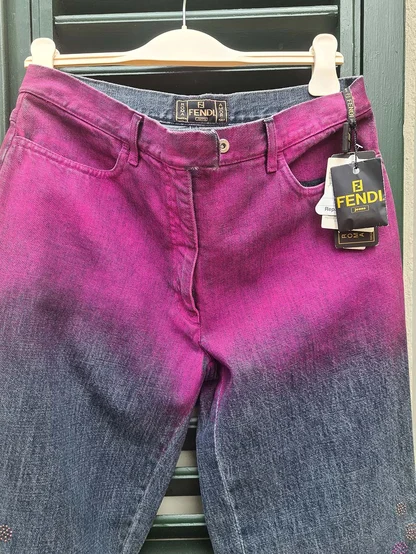 Fendi jeans fading from magenta to blue, hanging in front of green shutters with the swing tag attached