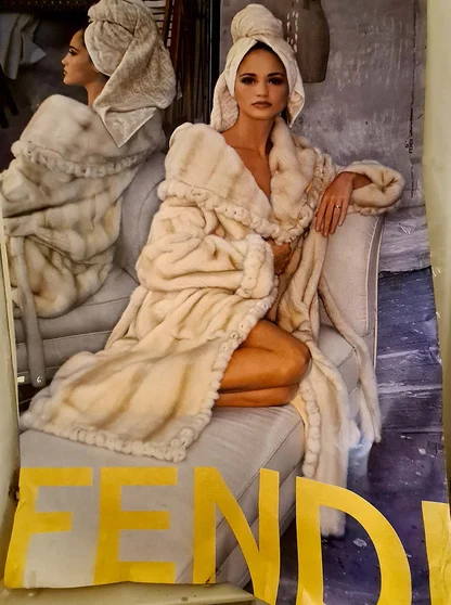 Vintage Fendi poster of a woman in a cream mink coat with her hair wrapped in a towel, seated on a sofa