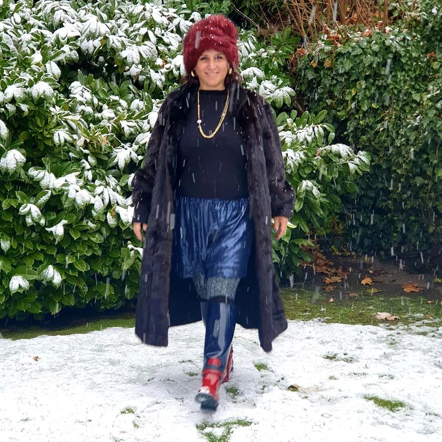 Gracie Opulanza walking through snow in a long black mink coat, blue pleated skirt and red boots, with a red fur hat