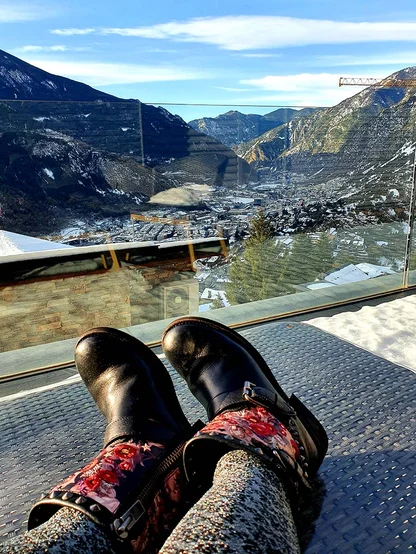 Black leather boots with red floral panels, feet up on a terrace overlooking a snowy mountain valley