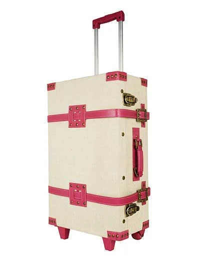 Cream canvas trolley suitcase with hot pink straps and corners, brass clasps and a pull-out handle