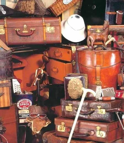 Heap of brown leather suitcases, a round hatbox, a white sun helmet and a Sprol oil can in an antiques display