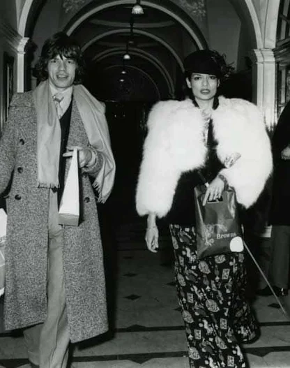 Mick and Bianca Jagger in 1973, she in a white fur jacket and printed trousers, he in a tweed overcoat and scarf