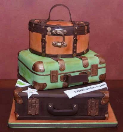 Novelty cake made to look like three stacked vintage suitcases in orange, green and dark brown with metal fittings