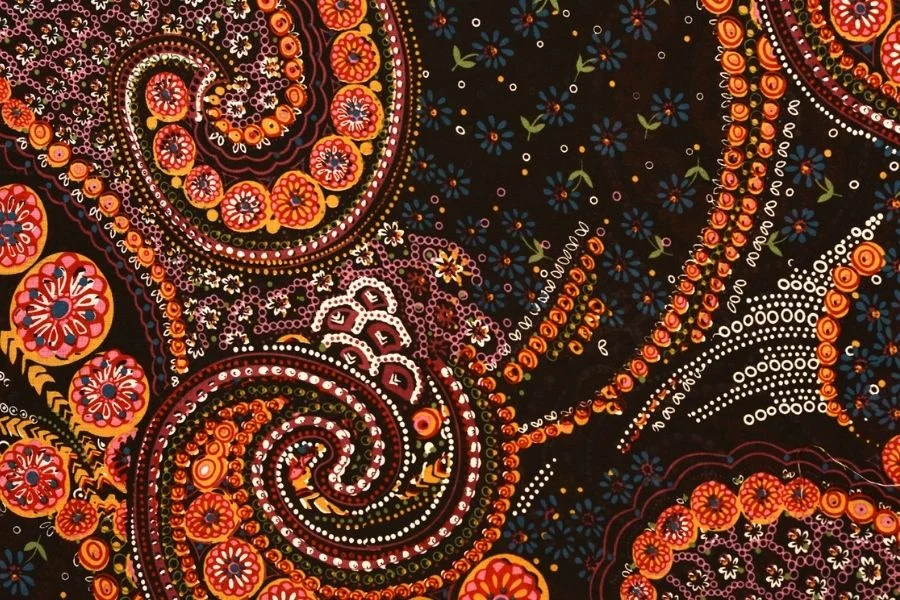 Close-up of a dark paisley print in orange, red and cream with small dotted swirls