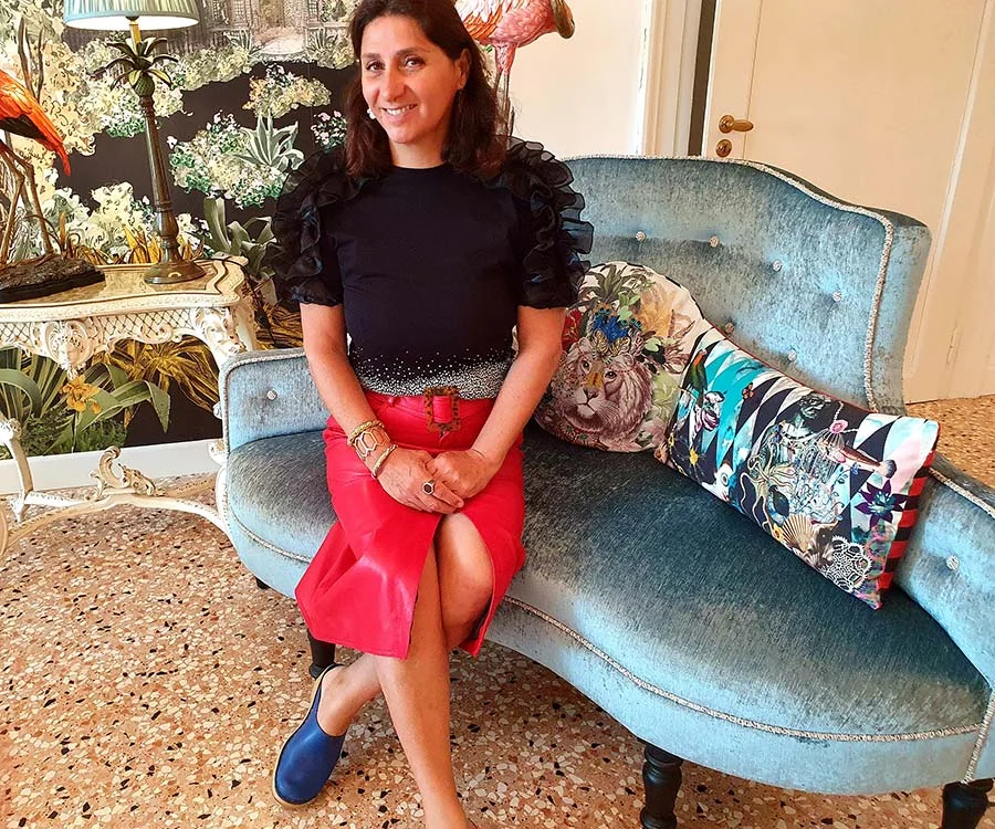 Gracie Opulanza in a red leather pencil skirt and black ruffle-sleeved top, seated on a blue velvet sofa in Venice