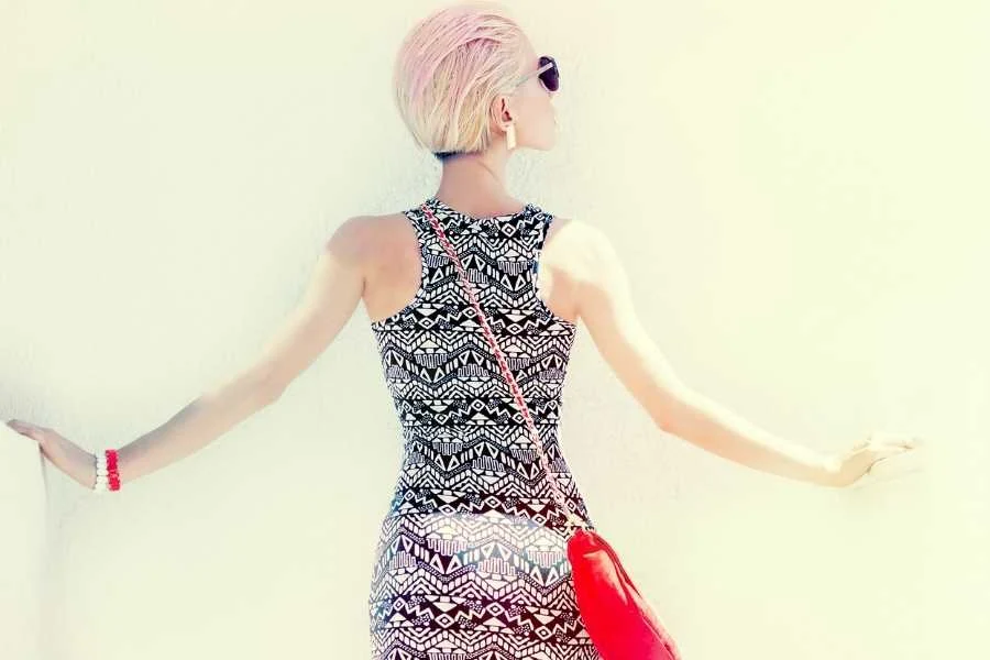 Back view of a woman with cropped blonde hair in a black and white zigzag print dress and a red tasselled shoulder bag