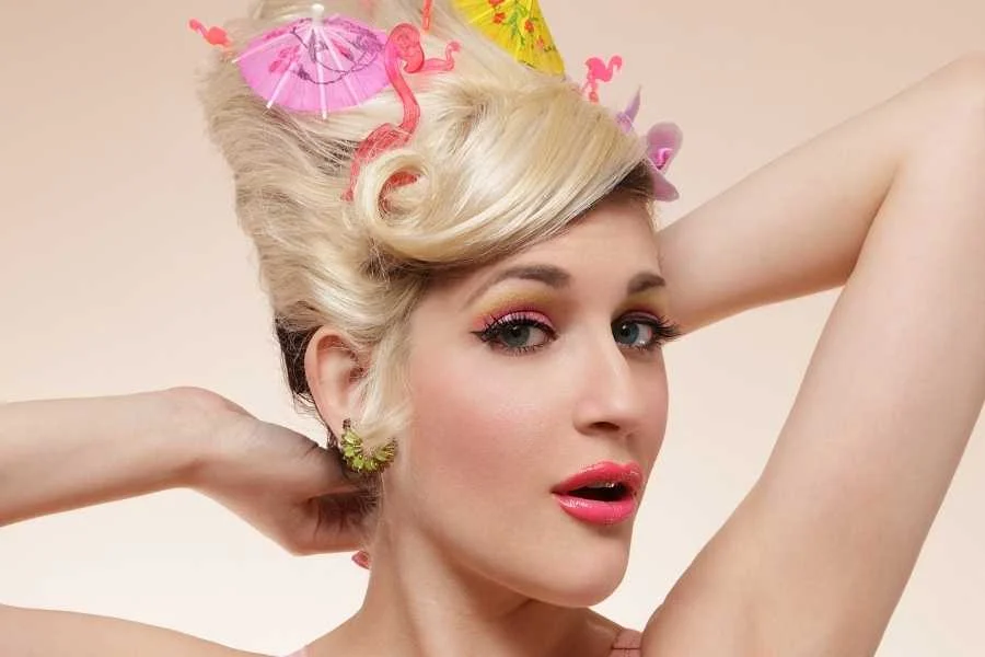 Woman with a high blonde beehive decorated with pink flamingo and cocktail umbrella hair accessories