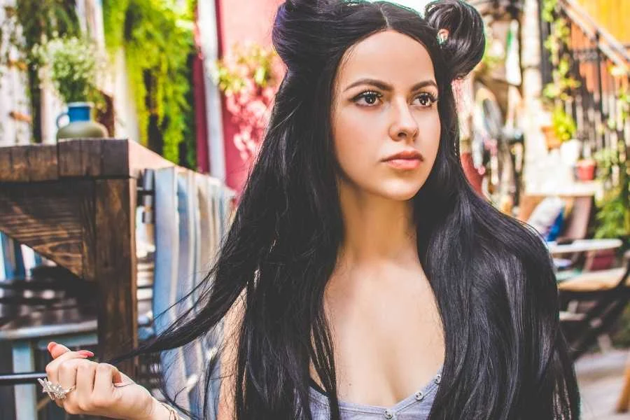 Woman with long black hair parted in the centre and two small rolls pinned at the crown, outside a café