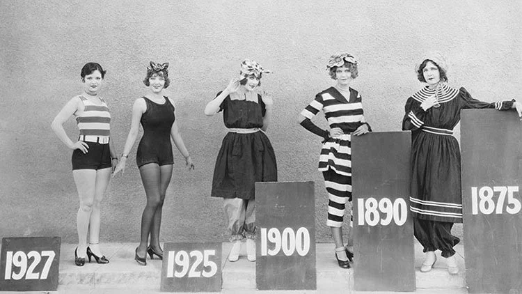 Black-and-white photograph of five women in bathing costumes dated 1927, 1925, 1900, 1890 and 1875, each beside a board