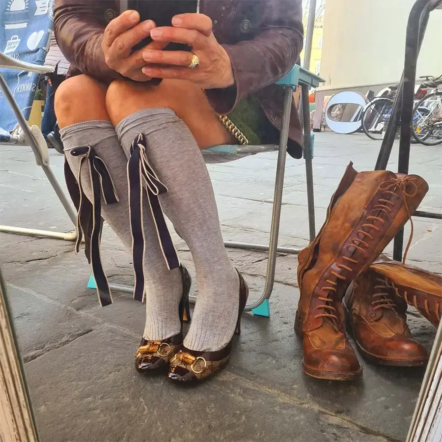 Gracie Opulanza in grey knee socks with ribbon ties and vintage Gucci shoes with gold-tone buckles, by brown lace-up boots