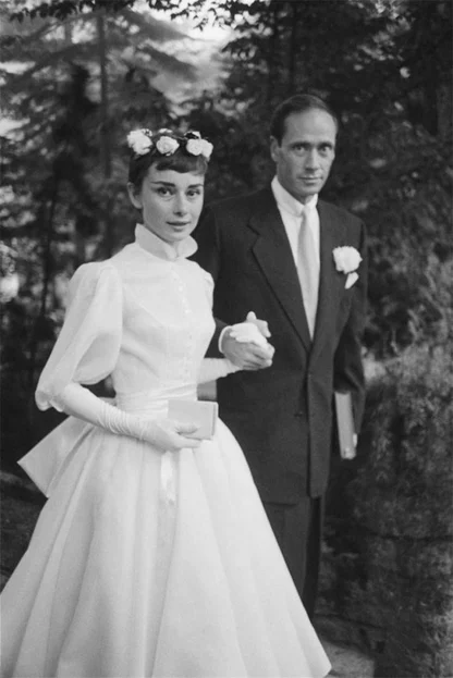 Black-and-white photograph of Audrey Hepburn in a white wedding dress with puffed sleeves, beside a man in a dark suit