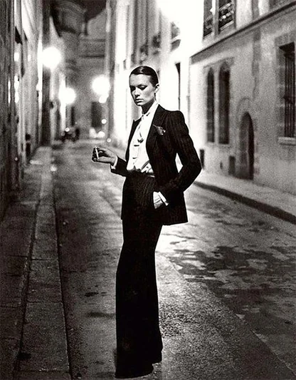 Woman in a black Yves Saint Laurent tuxedo suit, smoking on a lamp-lit street at night, 1966 photograph