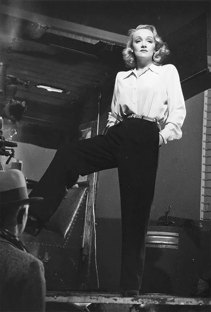 Two black-and-white photographs of a woman in a tailored tweed trouser suit and small hat, one beside an old car