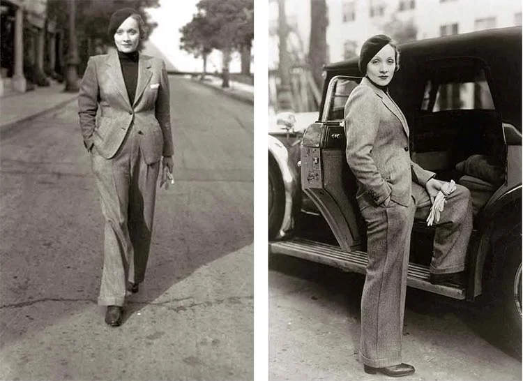 Marlene Dietrich in a white blouse and dark high-waisted trousers, one foot raised on a case, black-and-white photo