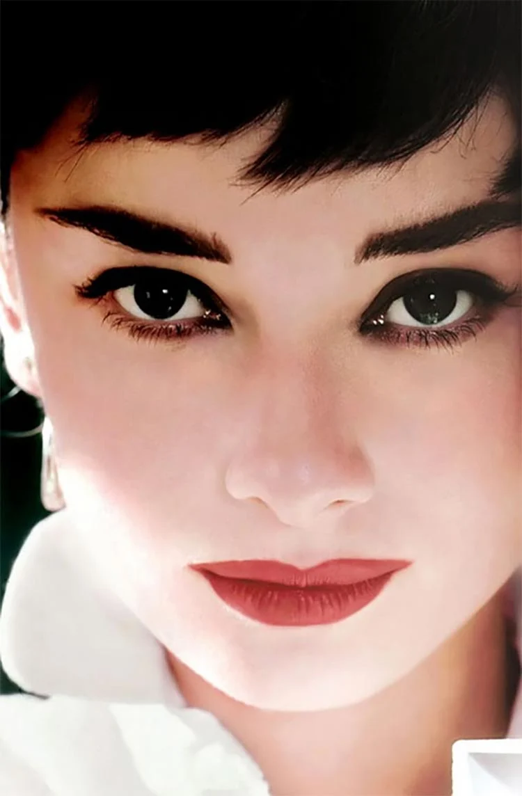 Close-up portrait of Audrey Hepburn with strong dark brows, defined eyes and red lips
