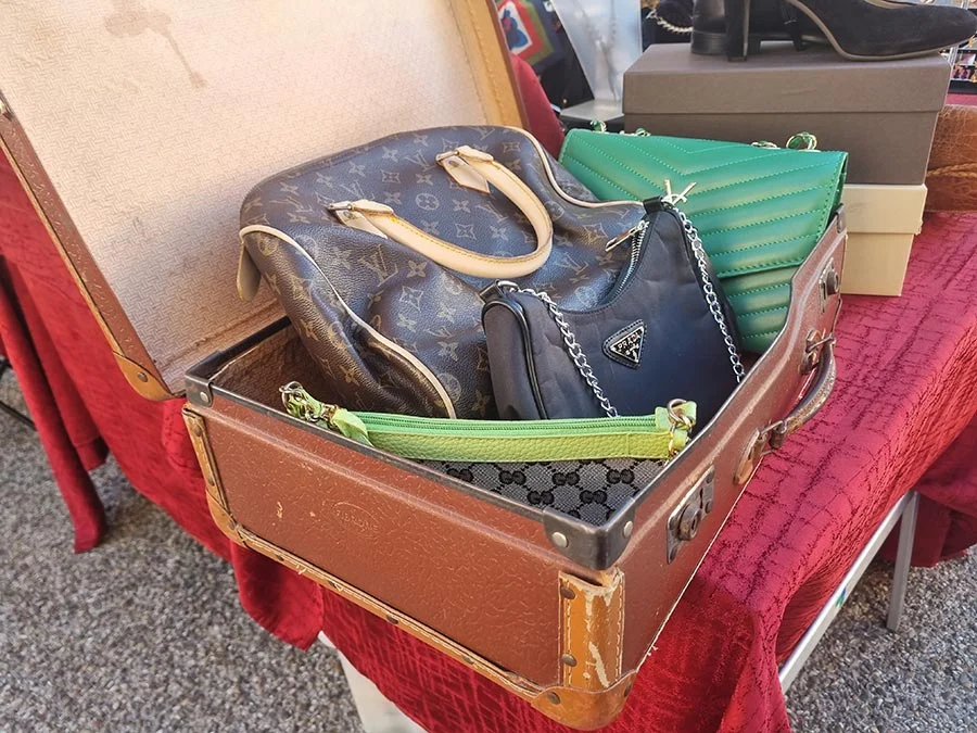 Open vintage suitcase holding a Louis Vuitton monogram bag, a small black Prada bag, a green quilted bag and a Gucci pouch