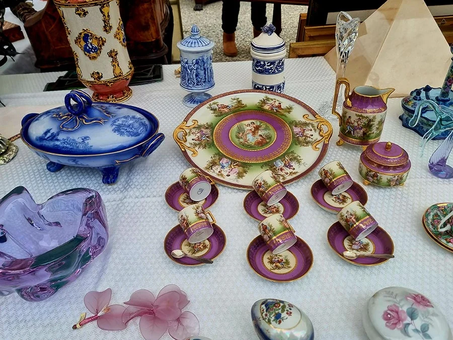 Market table of antique porcelain: a purple and gold coffee set, a blue tureen, blue and white vases and a mauve glass dish