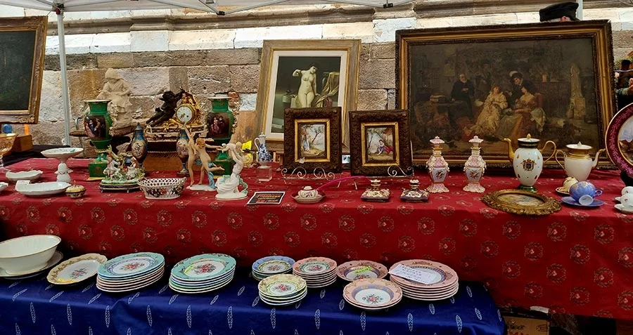 Antique dealer's stall on a red cloth with framed paintings, painted plates, vases and china figures