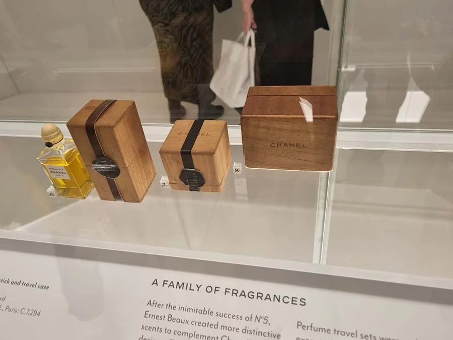 Chanel perfume bottle and two wooden travel boxes with black bands, in a case labelled 'A family of fragrances'
