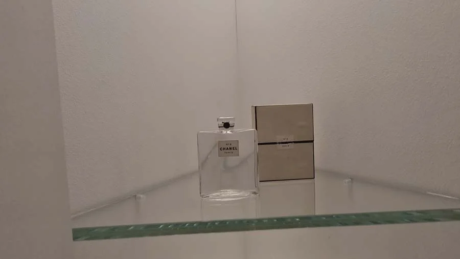 Glass Chanel perfume bottle and its cream box on a glass shelf in a museum case