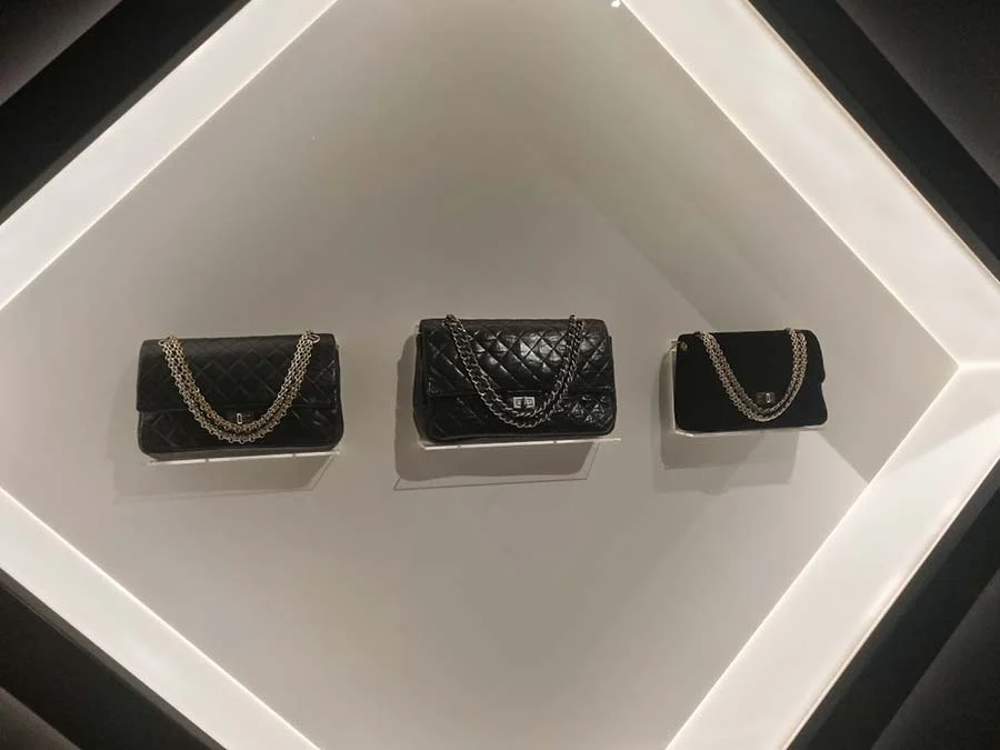 Three black quilted Chanel bags with chain straps, displayed in a lit white frame