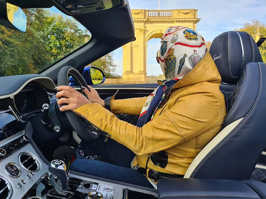Gracie Opulanza driving a Bentley GT Continental in a mustard leather jacket, a printed Hermès silk scarf over her hair