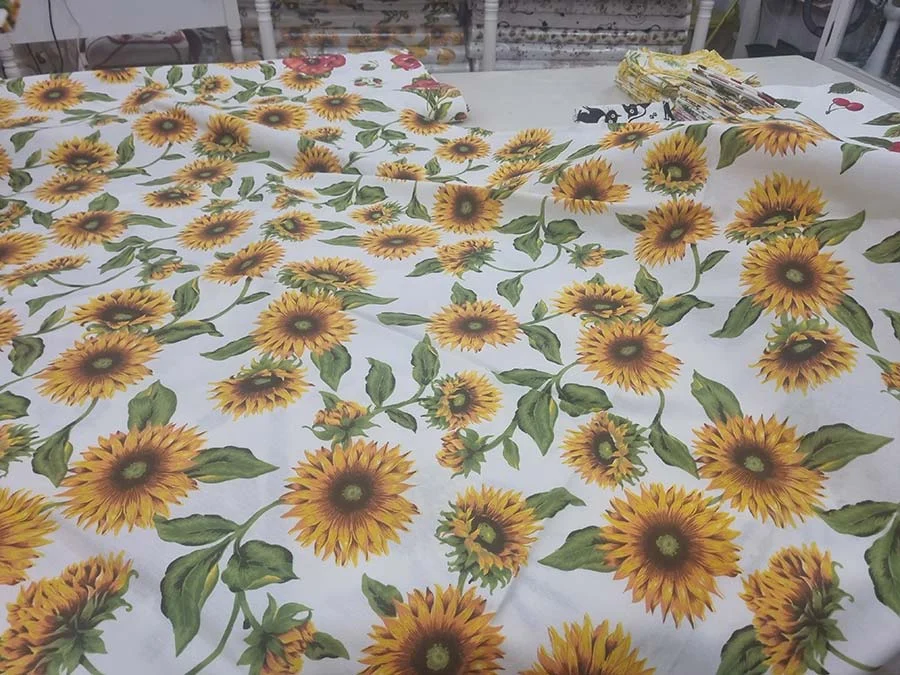 Cream fabric printed with large sunflowers and green leaves, spread flat on a shop counter